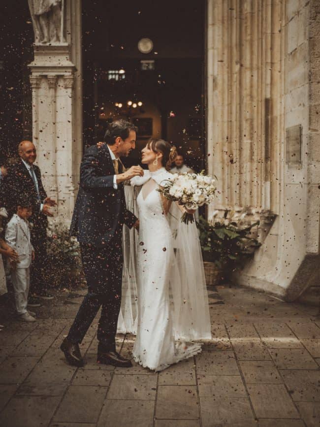 Sortie d'église pour les jeunes mariés. La mariée porte une robe de mariée sur mesure à encolure américaine en dentelle de Calais.
